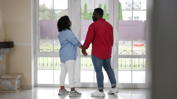 Back View Young Loving African American Couple Holding Hands Looking Out Glass Door Standing in New