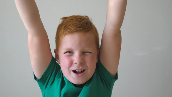 Adorable Handsome Red-haired Boy with Freckles Looking Into Camera and Raise Hands Rejoicing