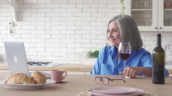 Happy Senior Mature Woman Drinking Wine Video Calling on Holiday Party at Home