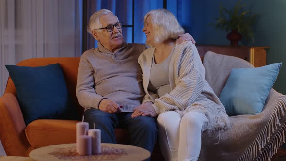 Happy Old Senior Elderly Family Couple Hugging Laughing Smiling Talking at Modern Home Sofa