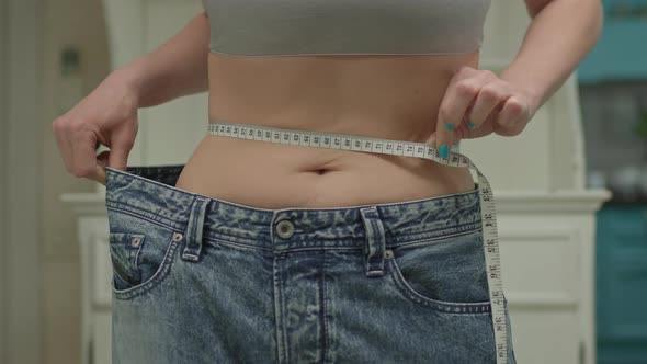 Close Up of Woman Measuring Her Waistline Wearing Oversized Jeans After Weight Loss