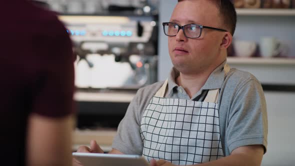 Caucasian man with down syndrome taking order in the cafe using a digital tablet. Shot with RED heli