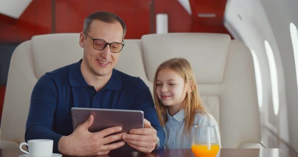 Father and Little Daughter with Digital Tablet Travelling By Private Jet