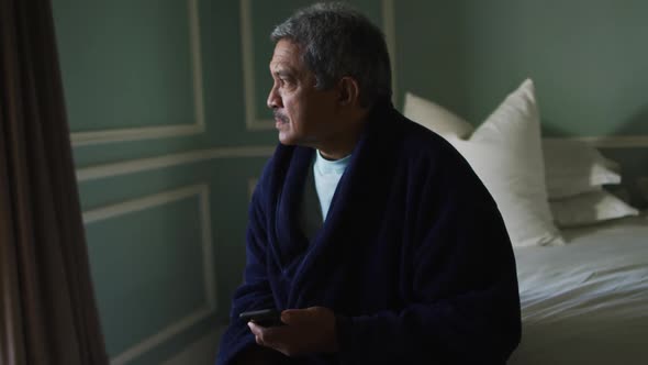 Senior mixed race man sitting on bed looking away