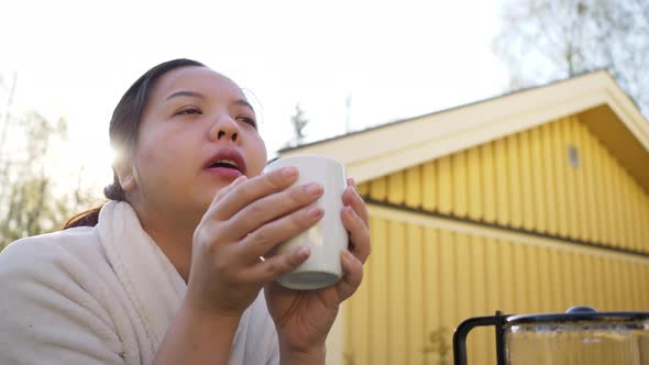 Asian woman holding and drinking hot coffee in front of her house in the morning