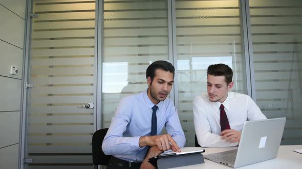 two young business man indoor office interior using personal computer and digital tablet, discussing