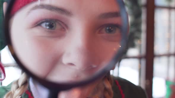 Cheerful elf girl looking at the camera through a magnifying glass. close-up