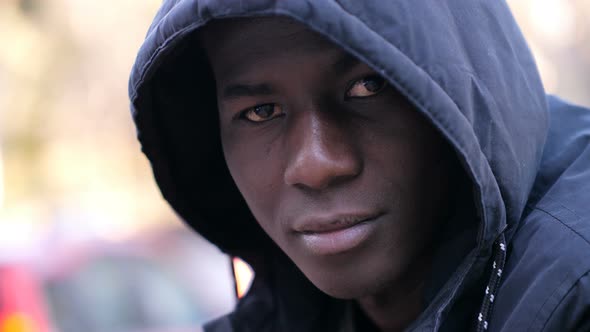 Thoughtful confident hooded young black african migrant looking at camera in the street