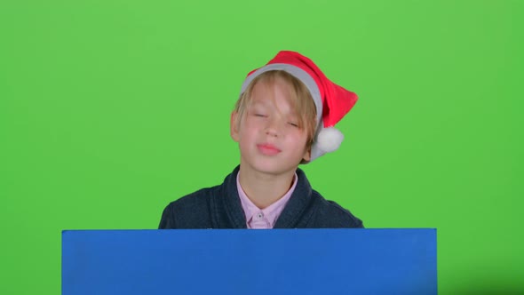 Child Boy Peering Out From Behind Blue Poster Waves a Hand in Front of Green Screen