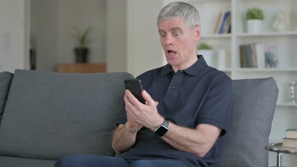 Middle Aged Businessman Having Loss on Smartphone on Sofa