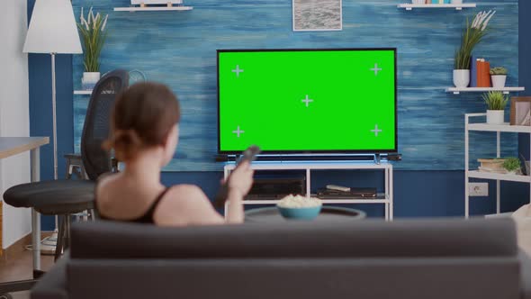 Young Woman Sitting on Sofa Looking at Green Screen on Tv and Switching Channels