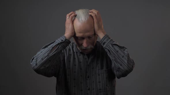 Grey Haired Senior Man Shakes and Holds Head with Hands