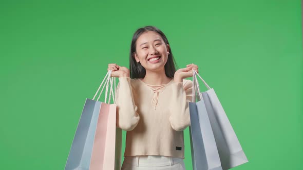 Happy Asian Shopping Woman With Shopping Bags While Standing In Front Of Green Screen
