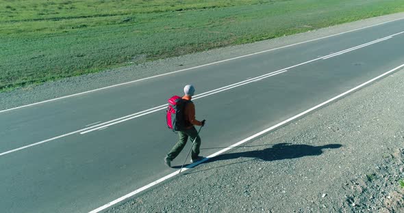 Flight Over Hitchhiker Tourist Walking on Asphalt Road. Huge Rural Valley at Summer Day. Backpack