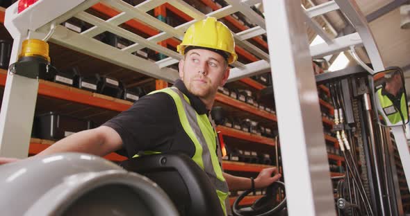 Caucasian male factory worker at a factory with a hat and high vis vest, using a truck