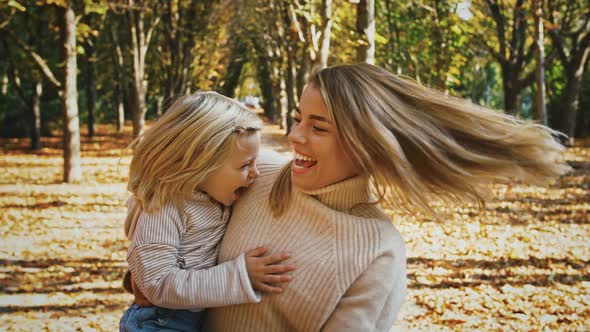 Young Mommy is Laughing Holding Little Daughter in Arms and Circling with Her Around Their Axis