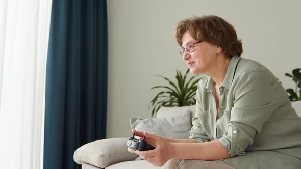 Senior Woman Gamer Sits on the Sofa Plays and Wins in Video Games on the Console