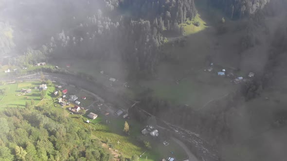 Flying Through the Clouds Over Carpathian Mountain Valley with Village in Summer
