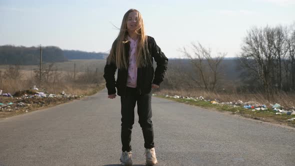 Cheerful Female Child with Long Blonde Hair Dances Funny on the Road at Countryside