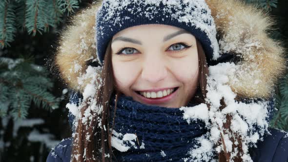 A Charming Girl with Snow on Her Hair and Head Looks at the Camera in a Snowy Forest