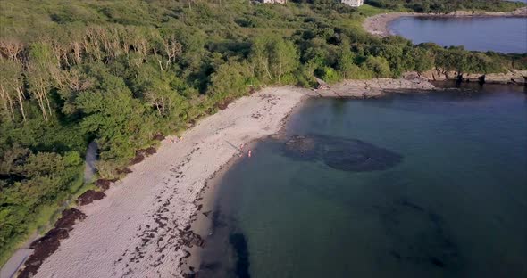 Aerial shot flying over a white sandy beach between the blue Atlantic Ocean and the lush green fores