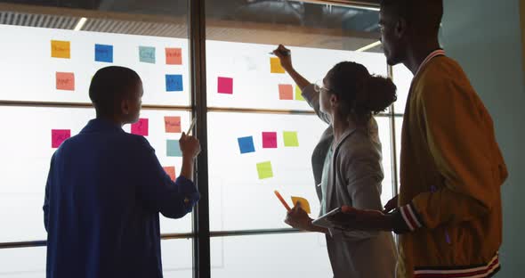 Diverse male and female creative colleagues brainstorming using tablet and writing on memo notes