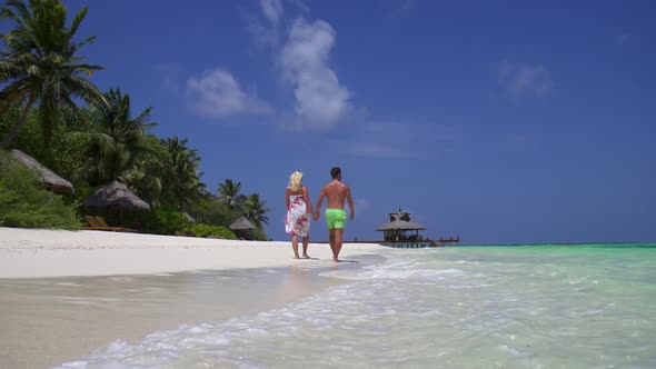 A couple walks on the beach holding hands at a tropical island resort hotel