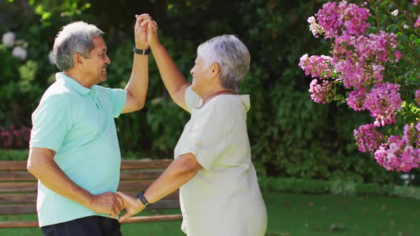 Video of happy biracial senior couple holding hands and dancing in garden