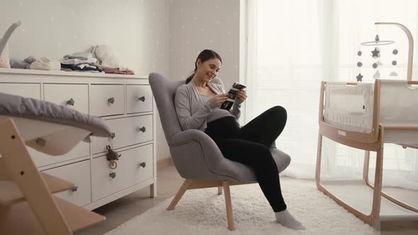 Wide shot video of caucasian woman in advanced pregnancy browsing ultrasound scan in baby's room.