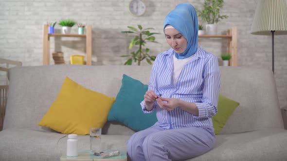 Muslim Young Pregnant Woman Taking Pills Sitting on the Couch