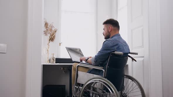 Bearded Guy which Sitting in Wheelchair and Remotely Working on Computer 
