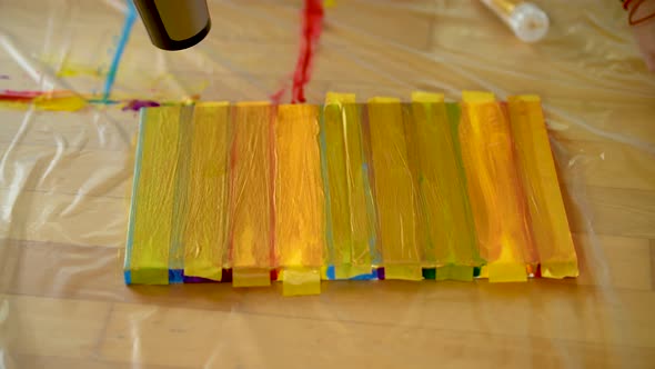 A woman using painters tape to finish her colorful stripes on a canvas