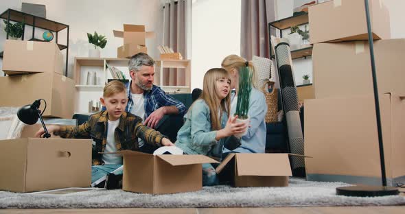 Family with Two Kids Sitting on the Floor Among Cardboard Boxes in Relocation Day