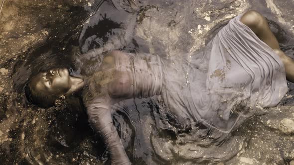 A Woman Is Lying in the Water Covered All Over with Gold Paint