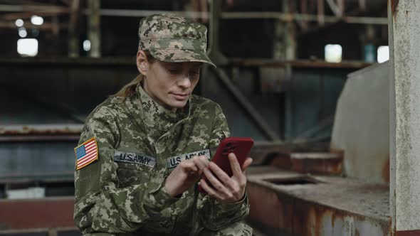 US Army Woman Typing on Smartphone in Destroyed Building