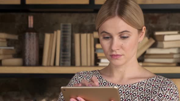 Good Looking Woman Using A Tablet near bookshelf. Beautiful girl touch computer