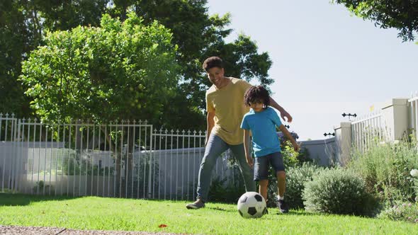 Happy biracial man and his son playing football in garden