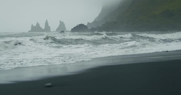 The Black Sand Beach of Reynisfjara with Waves Hitting the Shore on Foggy Rainy Stormy Day