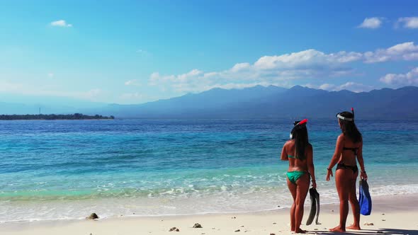 Snorkeling in the tropical ocean, two sexy ladies in the bikinis with snorkeling masks and fins talk