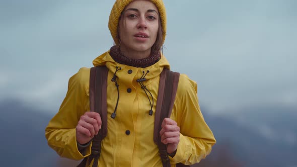 Close Up Portrait of Attractive Woman Hiker in Bright Yellow Raincoat and Beanie with Backpack