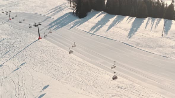 Profile drone shot of empty ski lifts over fresh ski slope