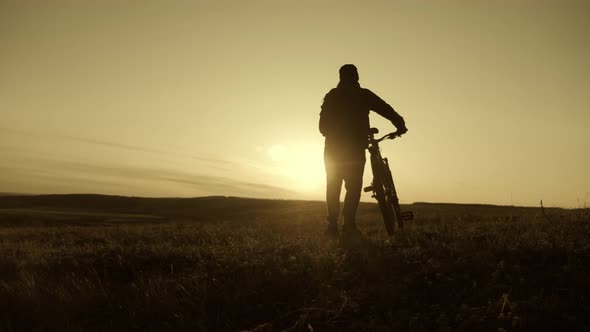 Silhouette of the Mountain Bicycle Rider on the Hill with Bike at Sunset. Sport, Travel and Active