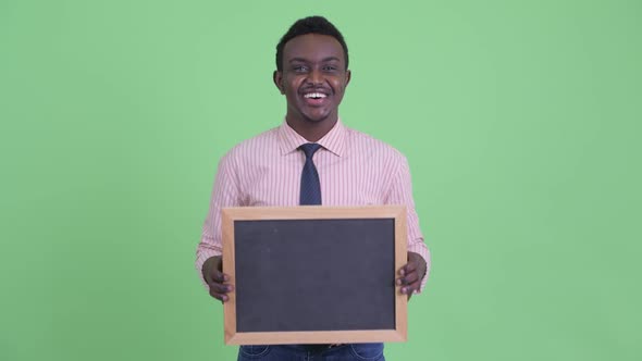 Happy Young African Businessman Holding Blackboard and Looking Surprised