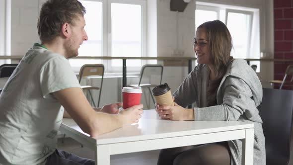 Two Friends are Sitting at the Table in Cafe Drinking Coffeetogo in Paper Cups and Talking