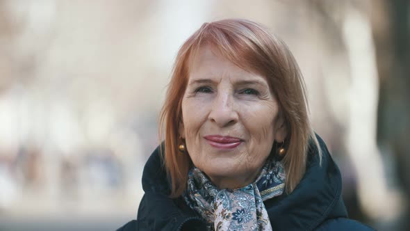 Happy Senior Woman in Trendy Scarf Standing in a Sunny Park in Autumn in Slo-mo  