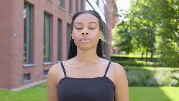 A Young Black Woman Looks Seriously at the Camera - an Office Building in the Background