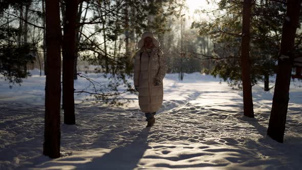 Happy Man in White Down Jacket is Walking in Snowy Park in Winter Between Naked Trees