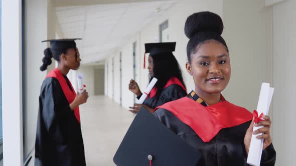 A Joyful Female Graduate with a Diploma in Hand Stands at the University Against the Background of