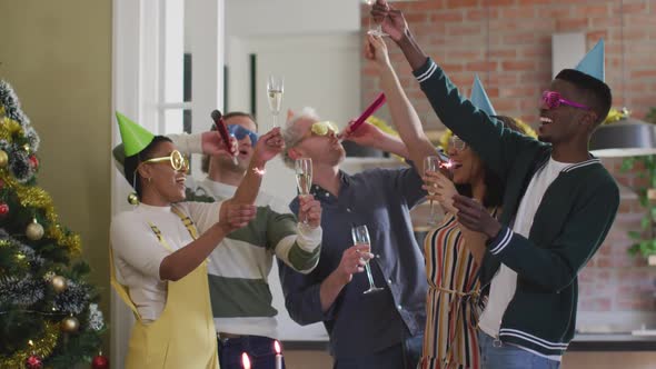 Happy group of diverse friends in party hats celebrating together, toasting with vine