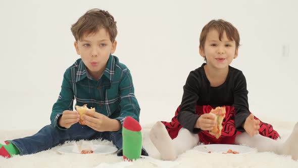 Two kids (boy and girl) eat hot dogs seating on the white carpet